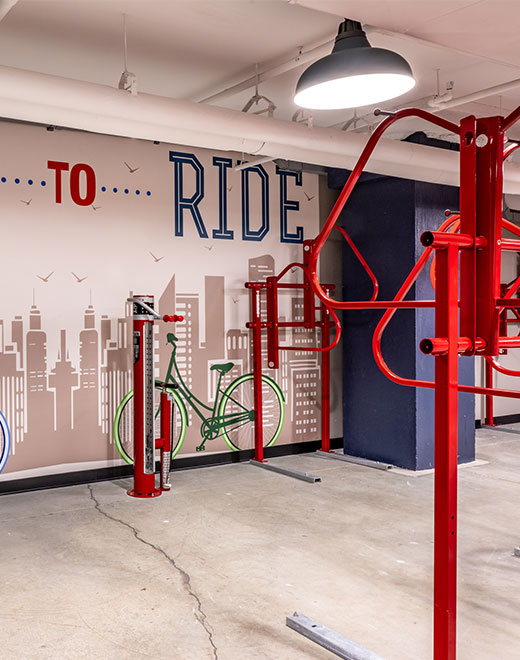 Gym with red exercise machine bars and a wall mural depicting a green bicycle on its side against light brown buildings